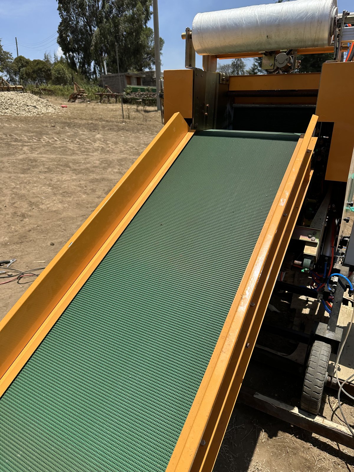 Close view of the green slat infeed conveyor and the clear inner film reel on the silage baler wrapper