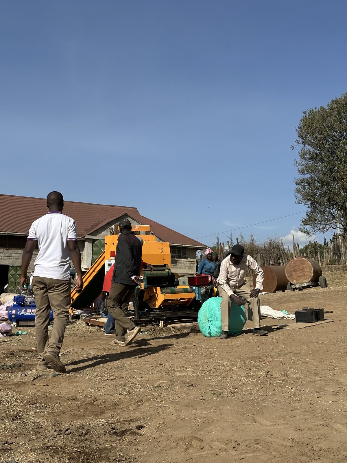 A finished green-wrapped round silage bale on the ground beside the baler wrapper and air compressor in Narok County